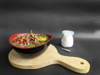 Spicy porridge served in a plastic bowl with a spoon. This dish is typical of Kalimantan, with a black background.
