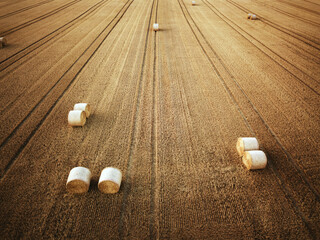 Aerial view of a harvested field with neatly placed round hay bales under warm evening light. The...