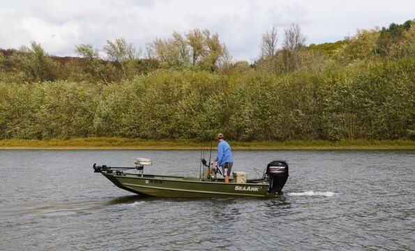 Susquehanna, Pennsylvania, U.S - Oct 19, 2025 - A fisherman steering a SeaArk jon boat equipped with a Mercury outboard motor and fishing gear