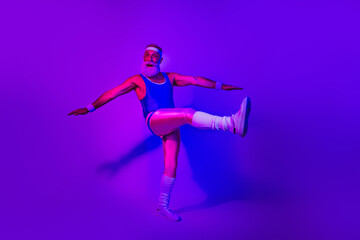 Energetic bearded senior athlete in a retro jumpsuit performing a dynamic kick under purple blue neon lights