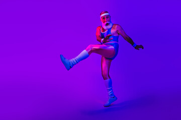 Energetic retro sportsman with beard in blue jumpsuit kicks mid air under neon purple studio lights and vibrant fashion vibe