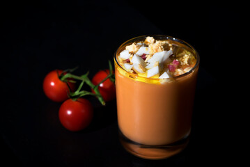 Vaso de salmorejo con tomate huevo jamon aceite y sal en fondo negro.