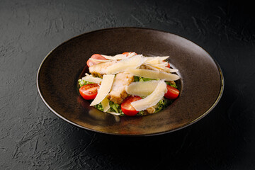 Delicious salad with chicken, tomatoes, and cheese on a dark plate