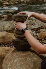 Close up of male hands stacking stones into a balancing tower on the bank of a mountain river. Symbol of harmony, balance, mindfulness, and relaxation in nature.
