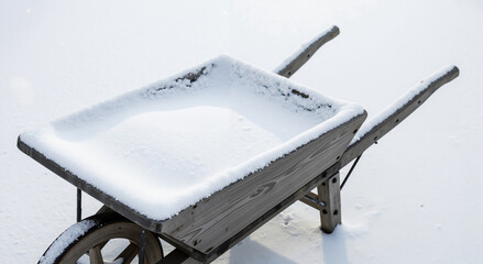 Wooden wheelbarrow filled with snow on a white background