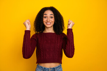 Confident young mixed race woman with curly hair wearing burgundy sweater smiles and raises her...