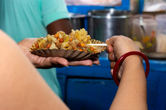 Bengali woman holding plate of alu kabli street food at roadside snacks stall in Kolkata