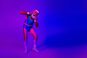 Elderly man in retro sportswear strikes a playful pose under purple and blue neon lights creating a fun energetic fitness lifestyle stock photo