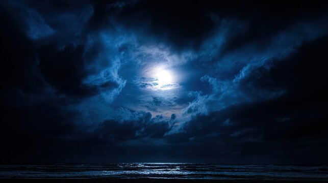 Full moon amidst dramatic dark clouds, over moonlit ocean waves at night, coastal seascape with atmospheric sky, wide angle view, copy space.