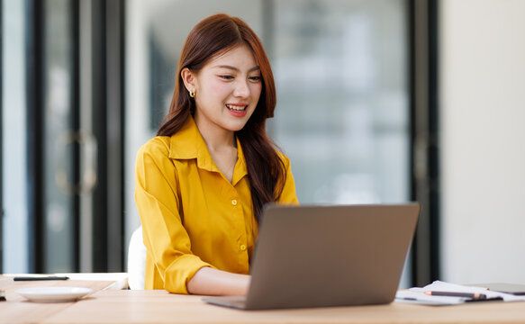 Smiling woman analyzing financial data graphs, charts on laptop display at a modern workspace. Financial analysis or business evaluation concept
 - Powered by Adobe
