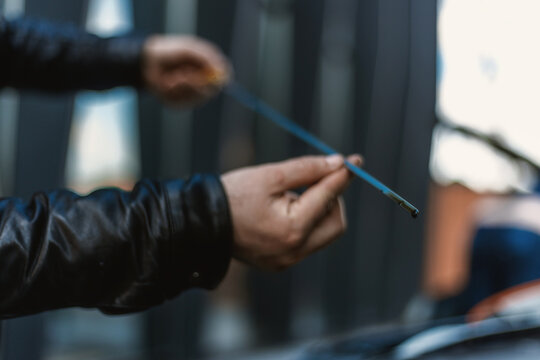 A close-up of a person's hand removing the oil dipstick from the engine. Routine maintenance, self-diagnosis, car care. The hand and the yellow dipstick are the main focus. Checking the oil level.