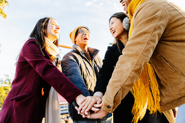 Cheerful young students joining hands in unity, enjoying the winter season outdoors while laughing...