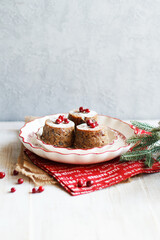 Three mini Christmas puddings decorated with cranberries and sugar powder on white festive plate with fir branches and red napkins over white wooden background. Side view, copy space