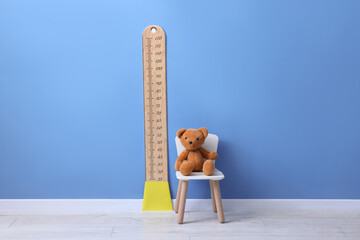 Height measuring chart on blue wall and toy bear indoors