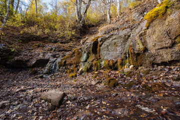 A stream flows through rugged rocks in peaceful woods, creating a picturesque landscape that attracts nature lovers and hikers seeking adventure and tranquility away from daily life