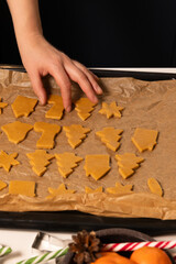 A person is placing gingerbread cookie shapes on a parchment-lined baking tray. The festive activity is taking place in a warm kitchen, filled with holiday spirit as preparations for Christmas begin.