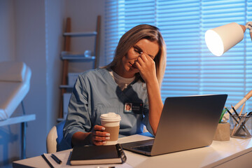 Tired doctor with coffee at table in clinic during night shift