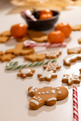 Gingerbread cookies, clementines, and candy canes are scattered on a white surface. The cookies are shaped like gingerbread men and stars, some with white icing.