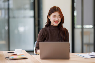 Smiley young business asian woman executive feeling happy about financial work results, corporate goals achievement getting new job offer sitting with laptop in office.
