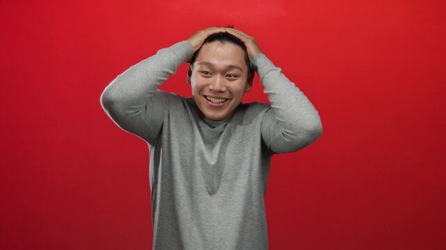 Young man expressing emotions with hands on head against an isolated red background wall.