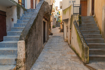 Narrow stone alleyway with aged staircases in a quaint european village. Baska, Krk island, Croatia