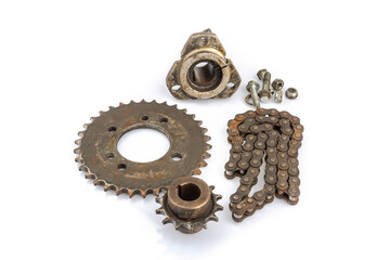 A close-up of a dirty, oily, and greasy chain, sprockets, and wheel hub on an old motorcycle against a white background. The image captures the essence of repair and maintenance.