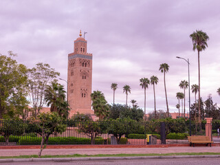 The iconic Koutoubia Minaret and vibrant palm trees create a stunning silhouette against a soft, lavender-hued sky in historic Marrakech, Morocco.