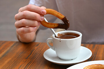 Person dipping a churro into thick Spanish hot chocolate at a café table