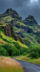 A winding road snakes through a lush valley nestled between towering, rugged mountains under a dramatic sky.