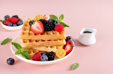 Sweet Belgian waffles with fresh berries and maple syrup on pink background. Top view. Desserts. 