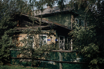 Abandoned rustic wooden house overgrown with trees and vines, behind a chain-link fence &mdash; perfect for themes of decay, nostalgia, mystery, and nature reclaiming man-made structures.