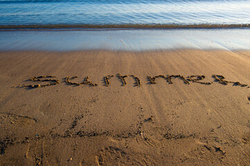 The word “Summer” written on sandy beach near the shoreline
