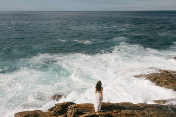 Woman in White Dress Overlooking Ocean from Rocky Shore