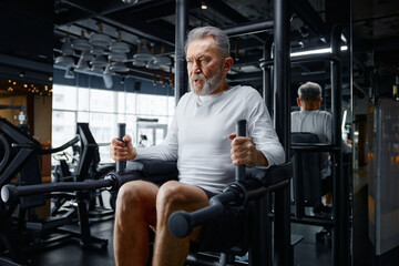 An older gentleman is actively exercising on a machine at a gym