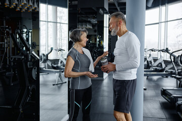 Mature man and woman are having a conversation while resting in a gym