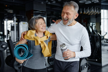 Elderly woman and man are standing, enjoying their gym day, sharing smiles together