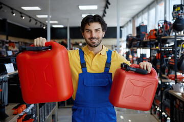 A man is holding two bright red gas cans in a workshop