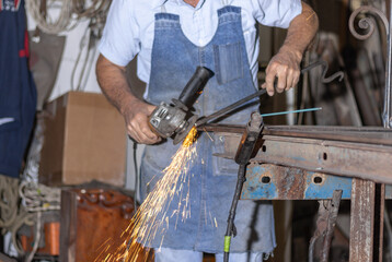 Man wearing an apron grinding metal in a workshop, sparks flying, shaping iron with an angle grinder