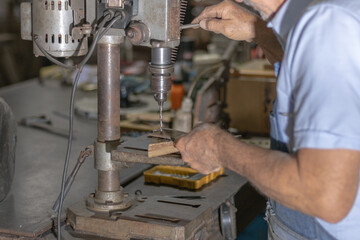 Metalworking craftsman drilling holes in a metal sheet using a vintage drill press in a workshop