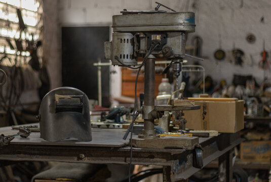 Workshop tools on a bench, a vintage drill press and welding helmet illustrating concepts of craftsmanship, repair, and industry