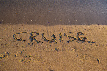 Fototapeta premium The word “Cruise” written on sandy beach near the shoreline