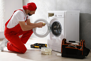 Professional repairman fixing broken washing machine indoors
