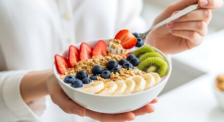 Person holding bowl of yogurt with strawberries blueberries kiwi and bananas fruit
