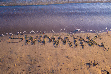 Fototapeta premium The word “Swimming” written on sandy beach near the shoreline