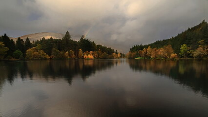 Glencoe Lochan surrounded by tall Canadian redwoods and Douglas firs planted in the 1890s, under a cloudy rainy sky with rainbow. Glencoe-Scotland-041