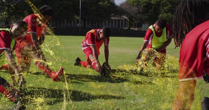 Stretching seven soccer players wearing red jerseys and colored bibs on grass field, with ball
