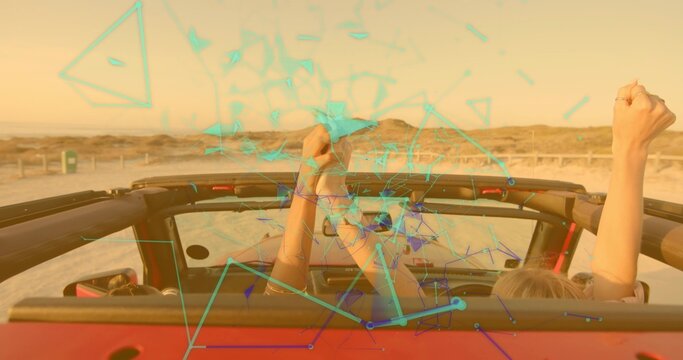 Driving two friends raising arms atop red convertible on coastal highway by rope fence golden hour