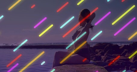 Sitting woman in swimsuit turning head facing ocean on rock ledge, with neon light streak overlays