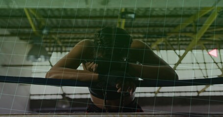 Leaning female boxer resting head on forearms over ring ropes inside boxing gym, showing sweat
