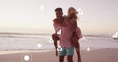 Walking man carrying woman in pink dress along ocean shore at sunset, with digital overlay icons